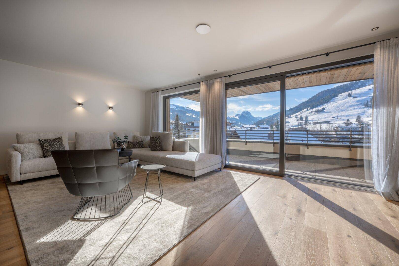 Helles Wohnzimmer mit Holzboden, bequemer Sitzecke und weitem Blick auf die verschneite Berglandschaft.