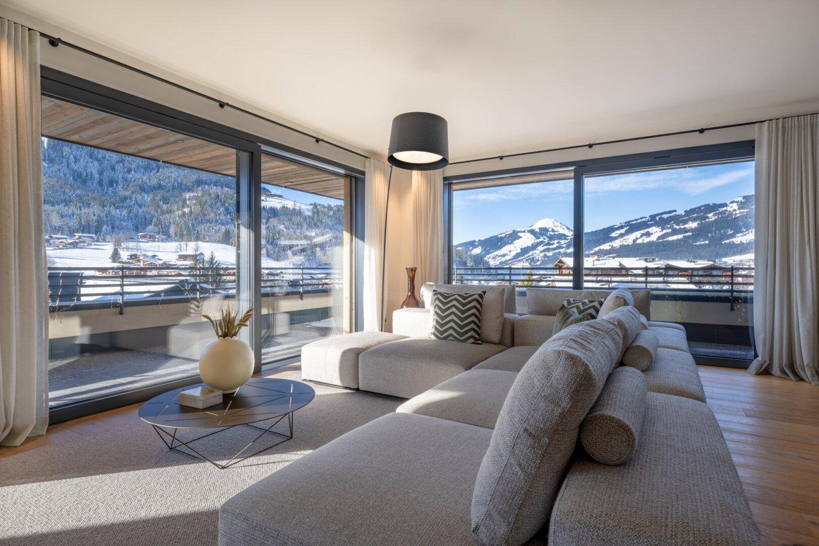 Gemütliches Wohnzimmer mit großem Sofa, stilvoller Beleuchtung und weitem Blick auf die verschneiten Berge.