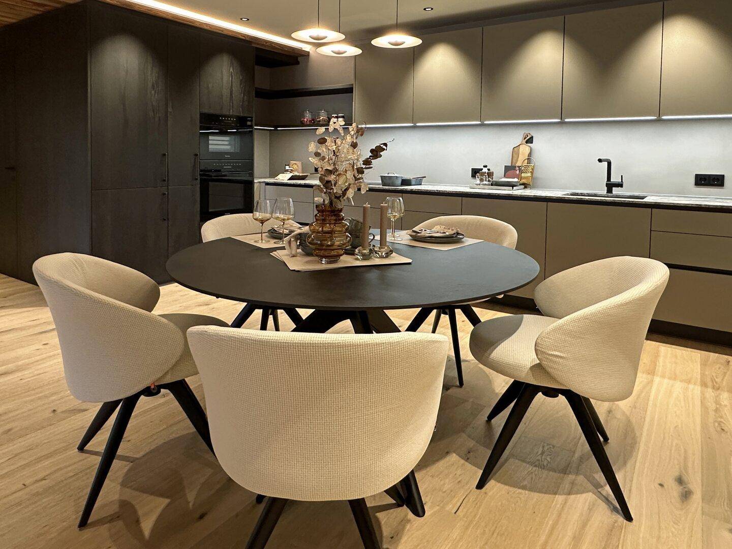 Moderne Küche mit runden Esstisch, hellen Stühlen und integrierten Geräten in schlichtem Design.