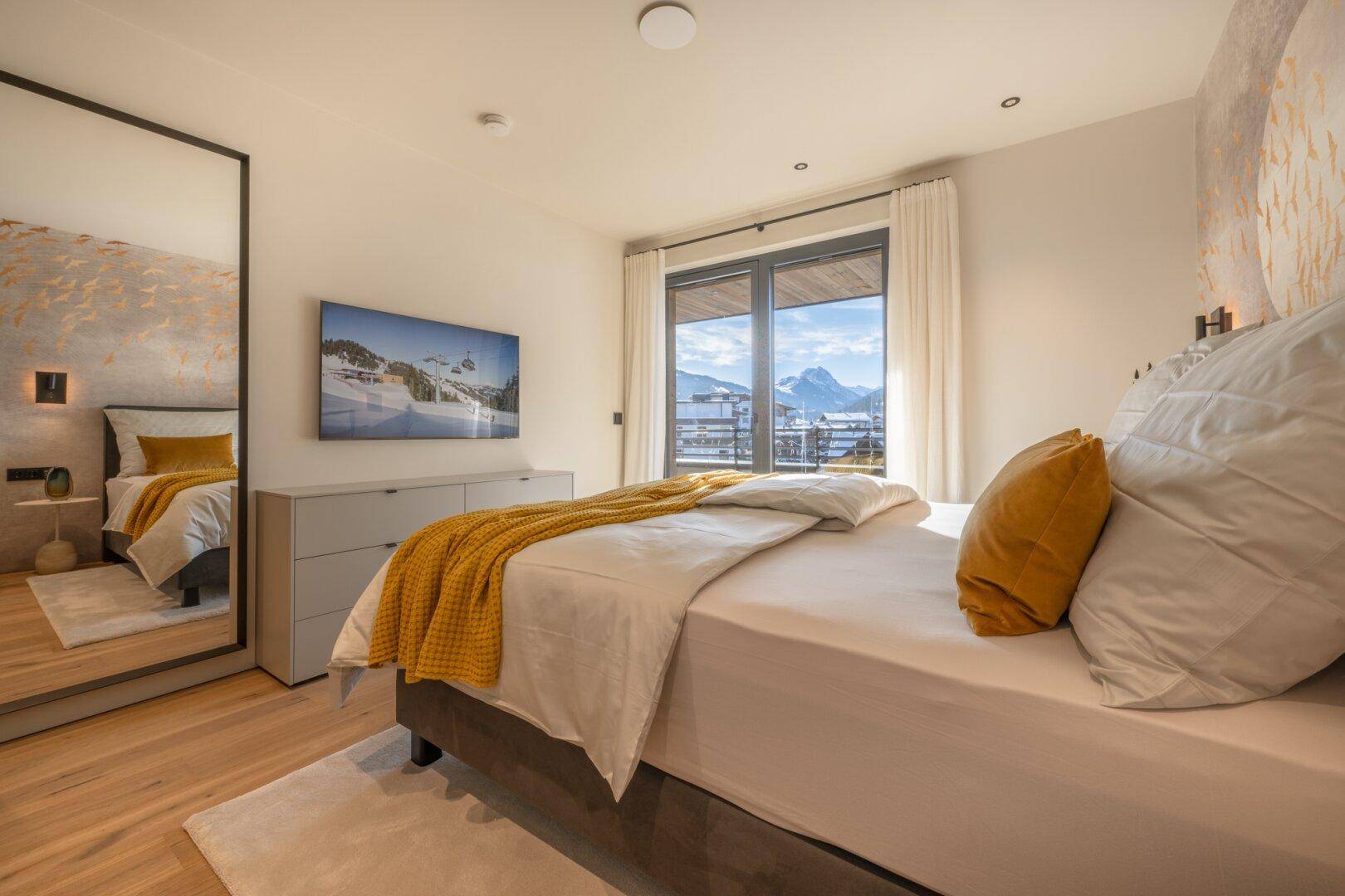 Gemütliches Schlafzimmer mit Doppelbett, großem Spiegel und Balkonzugang mit Bergblick.