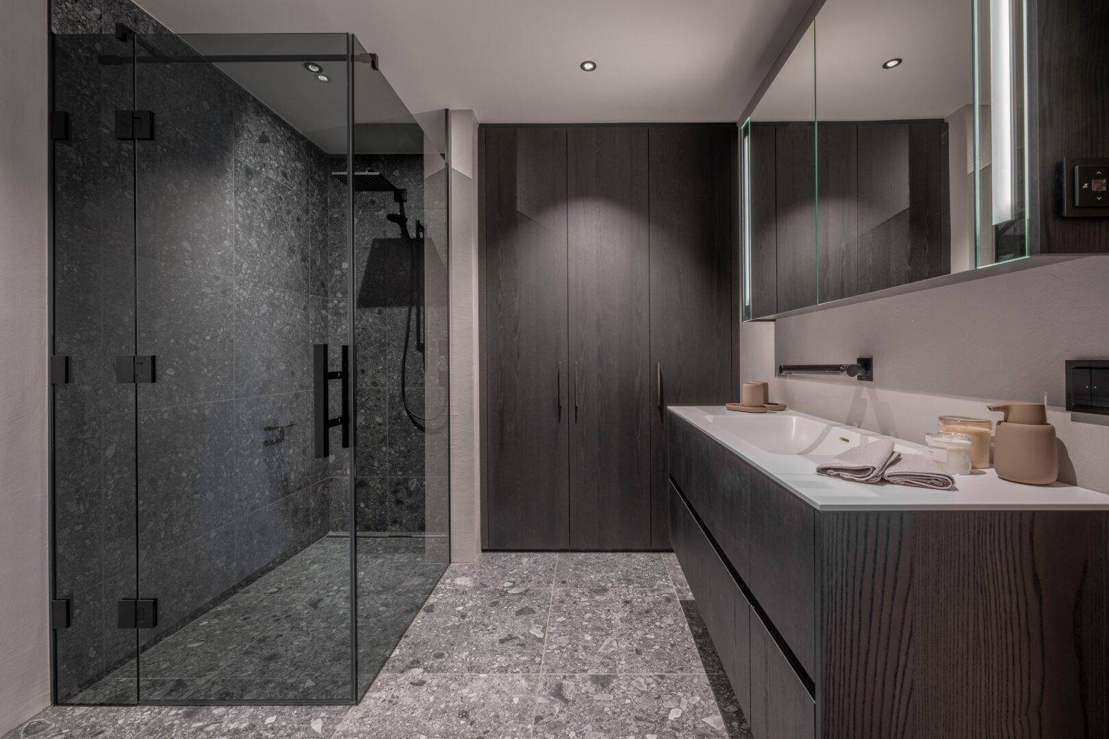 Modernes Badezimmer mit begehbarer Dusche, dunklen Fliesen und Doppelwaschbecken.