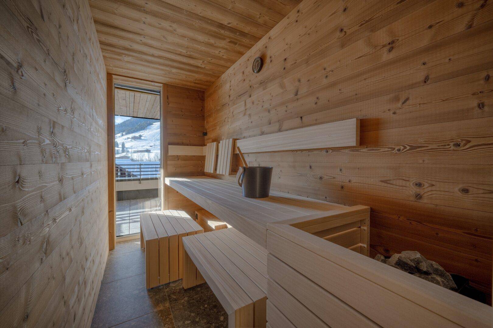 Geräumige Holzsauna mit Bänken und Blick auf die verschneite Landschaft durch ein Fenster.