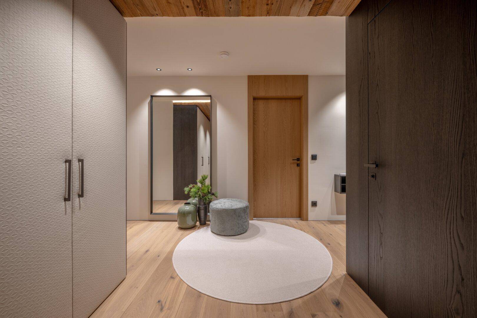 Heller Eingangsbereich mit Holzboden, Einbauschränken und dekorativem Hocker.