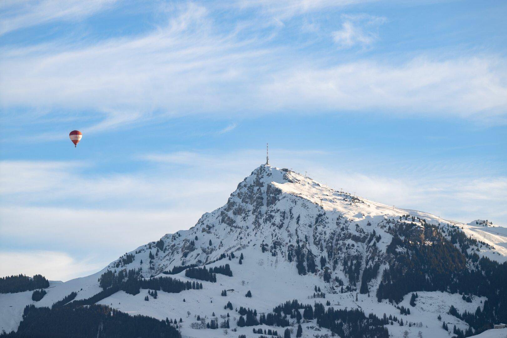 Majestätischer schneebedeckter Berg unter blauem Himmel mit einem Heißluftballon in der Ferne.