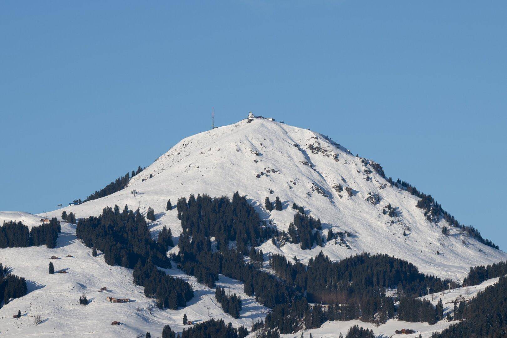 Beeindruckender schneebedeckter Berg mit Wald und klarem blauem Himmel im Hintergrund.