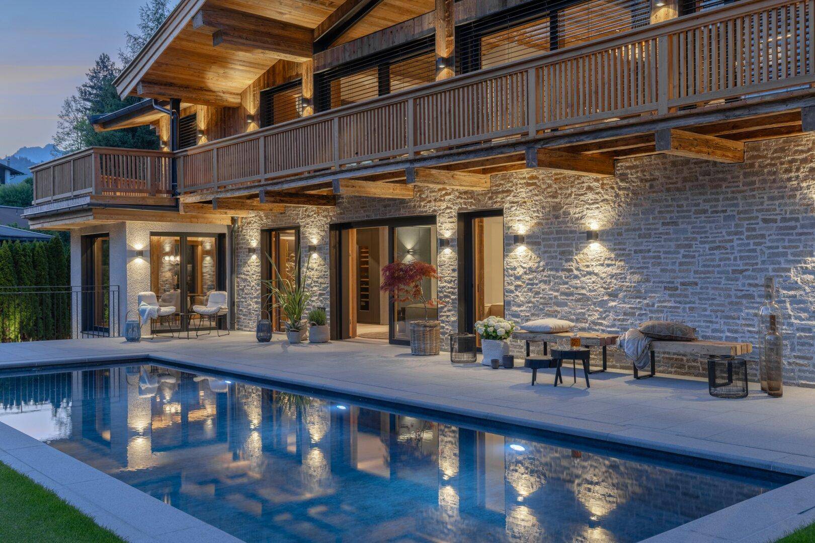 Abendliche Ansicht der luxuriösen Villa mit beleuchtetem Pool und gemütlicher Terrasse.