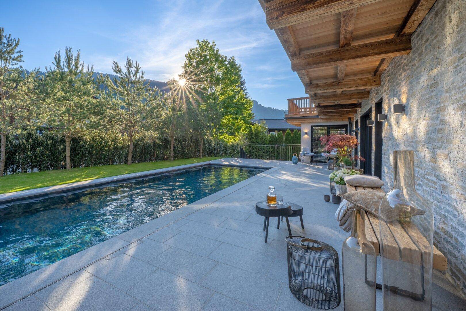 Sonnige Terrasse mit großem Pool, bequemen Sitzgelegenheiten und Blick auf die umliegende Berglandschaft.
