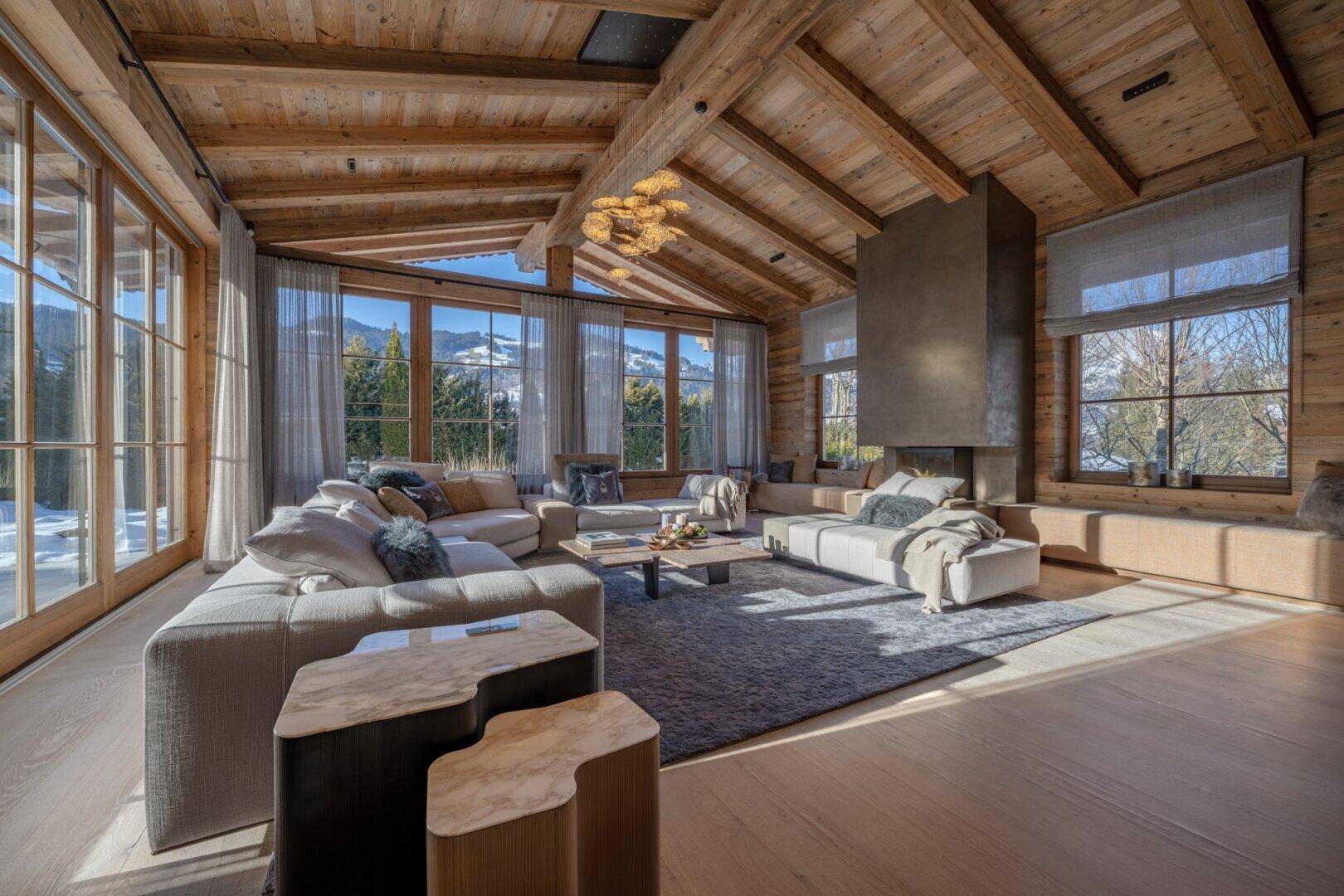 Geräumiges Wohnzimmer im Chalet-Stil mit Holzbalkendecke, Kamin und großen Fenstern mit Bergblick.
