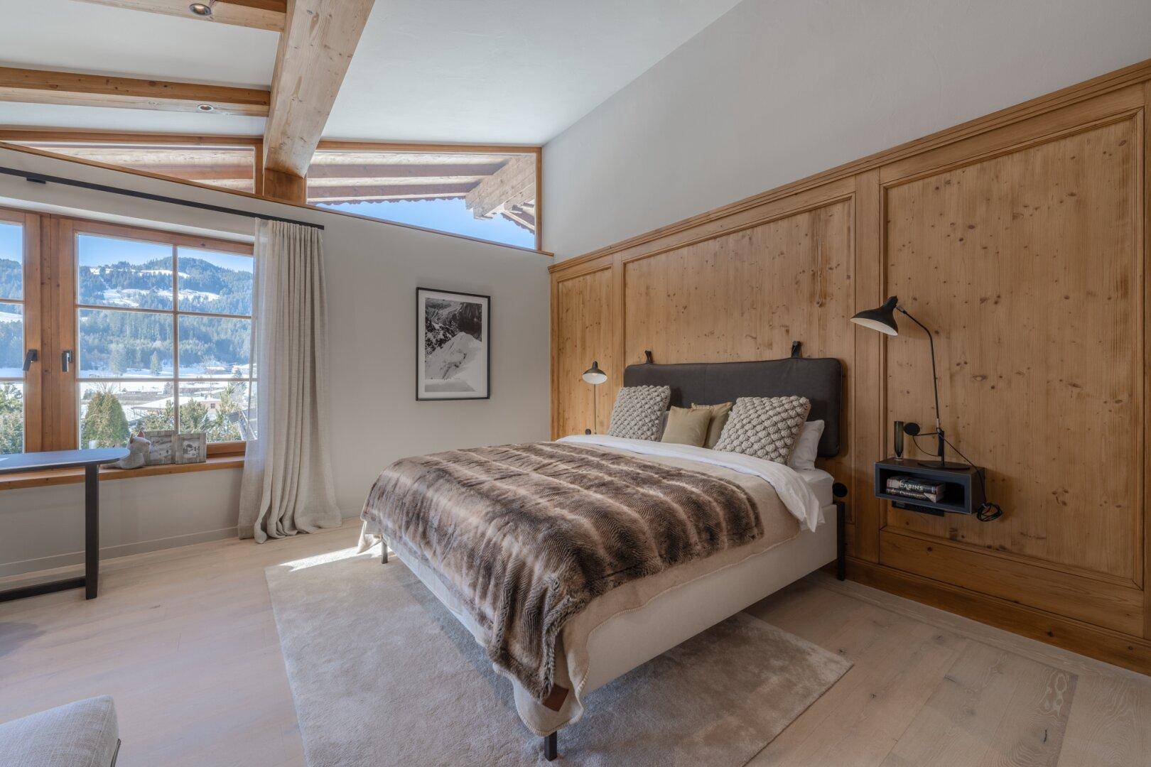 Gemütliches Schlafzimmer mit Holzwandverkleidung, großen Fenstern und Blick auf die verschneite Landschaft.