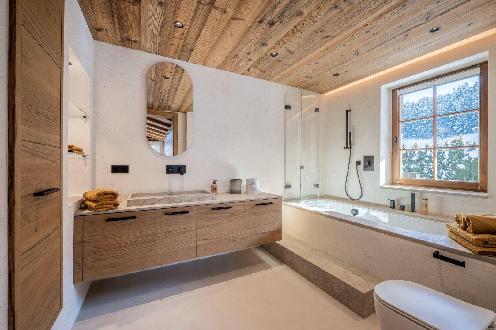 Modernes Badezimmer mit Holzwaschtisch, Badewanne und Dusche sowie Fenster mit Bergblick.