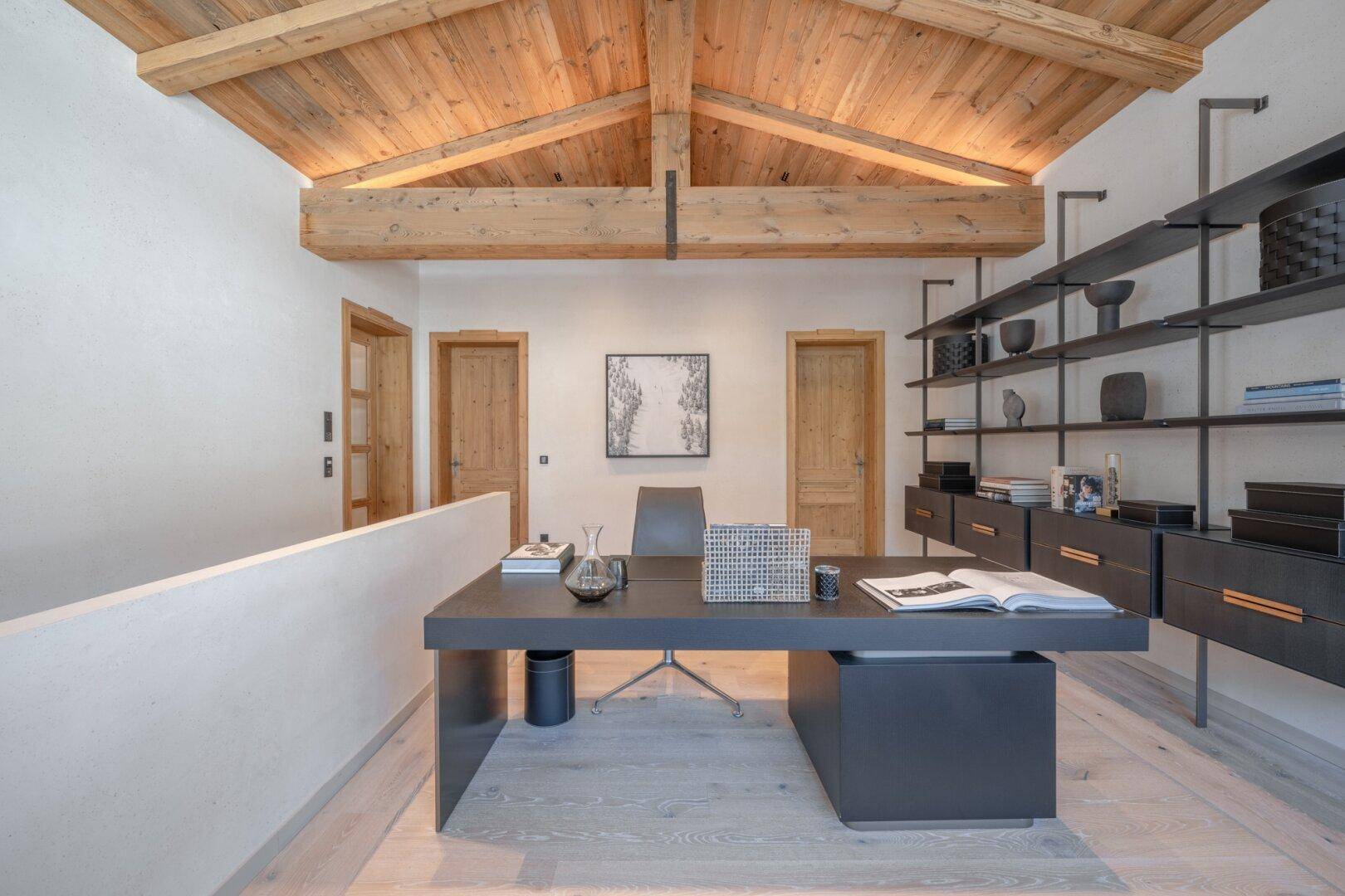 Offener Arbeitsbereich mit Holzbalkendecke, modernem Schreibtisch und integriertem Regalsystem.