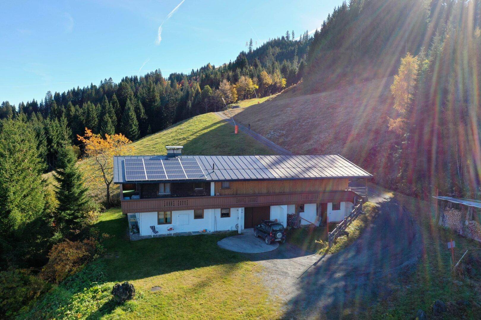 Haus in Hanglage mit Photovoltaikanlage auf dem Dach, umgeben von Wald und Wiesen.