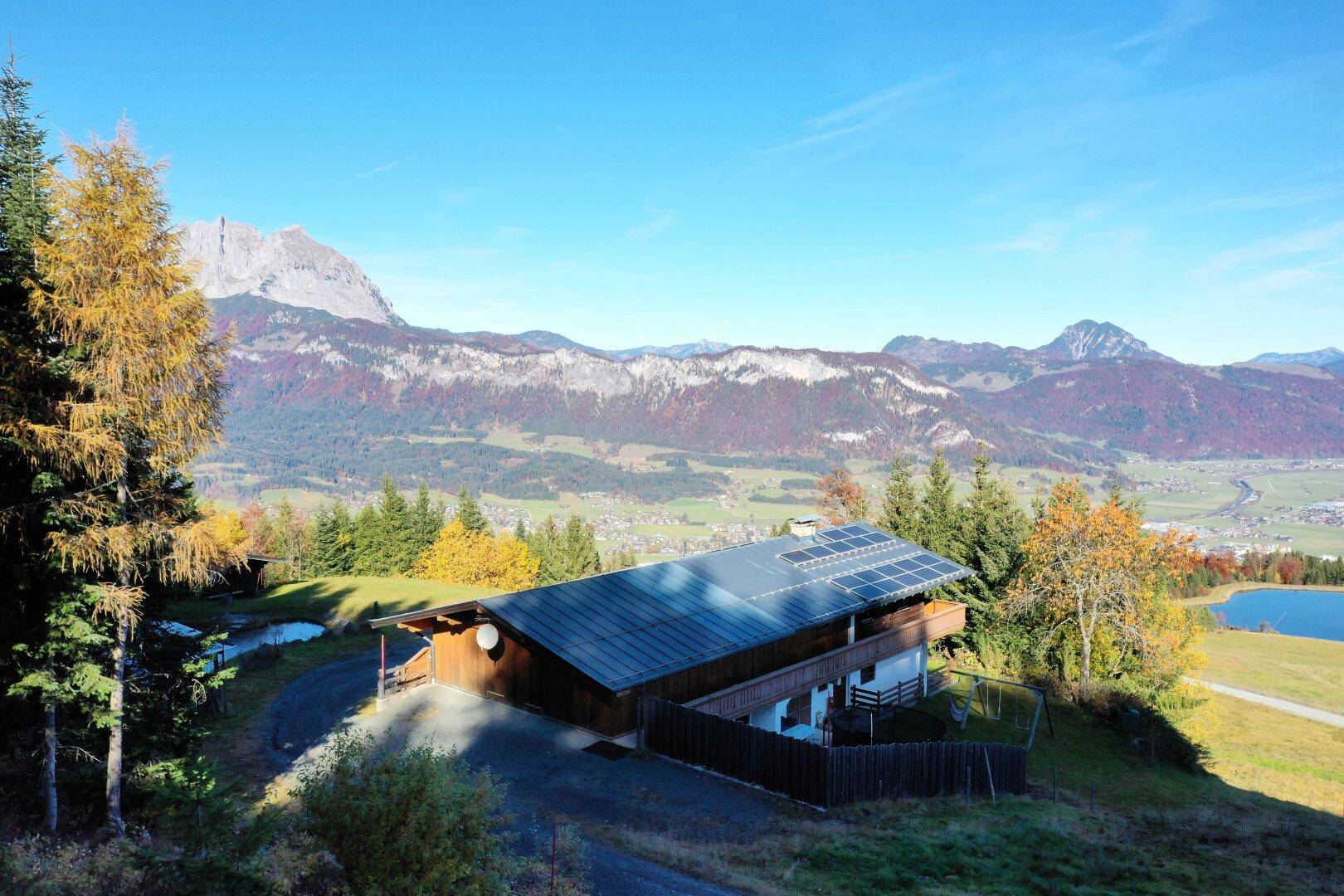 Idyllisches Haus in den Bergen mit Photovoltaikanlage auf dem Dach und weitem Blick auf die Landschaft und einen See.