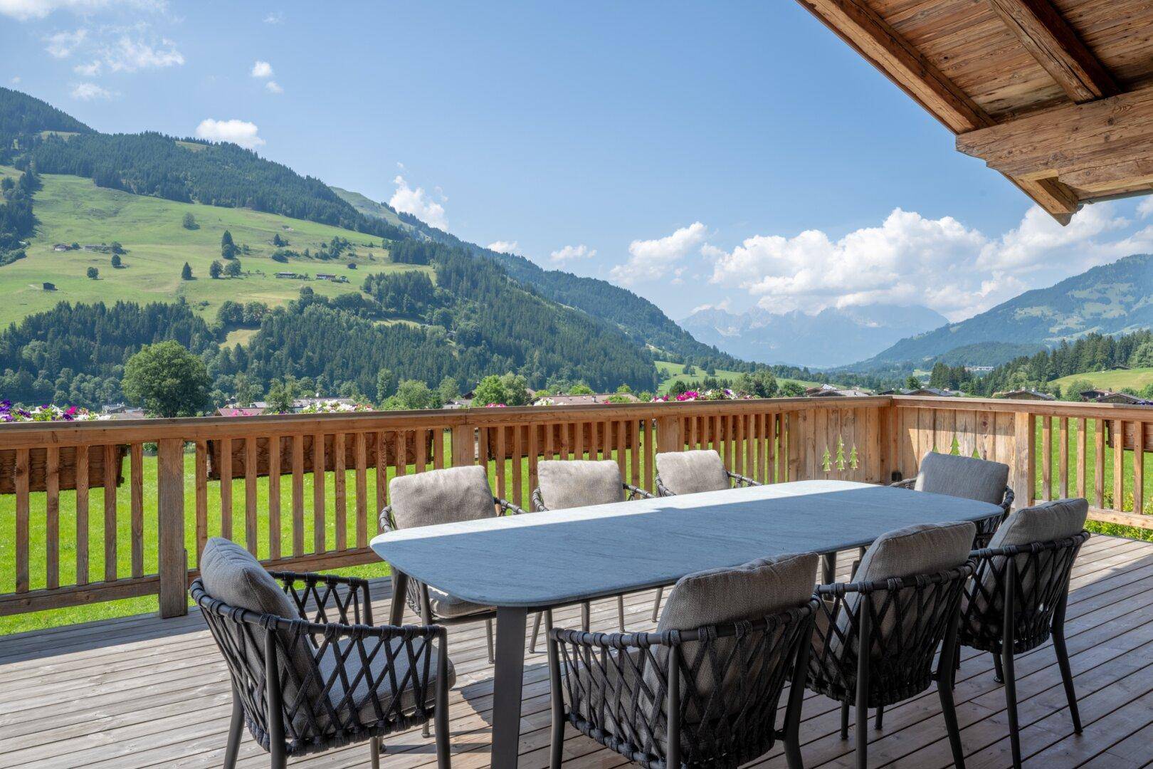 Detailansicht der Holzterrasse mit modernem Esstisch und bequemen Stühlen, umgeben von grünen Bergen.