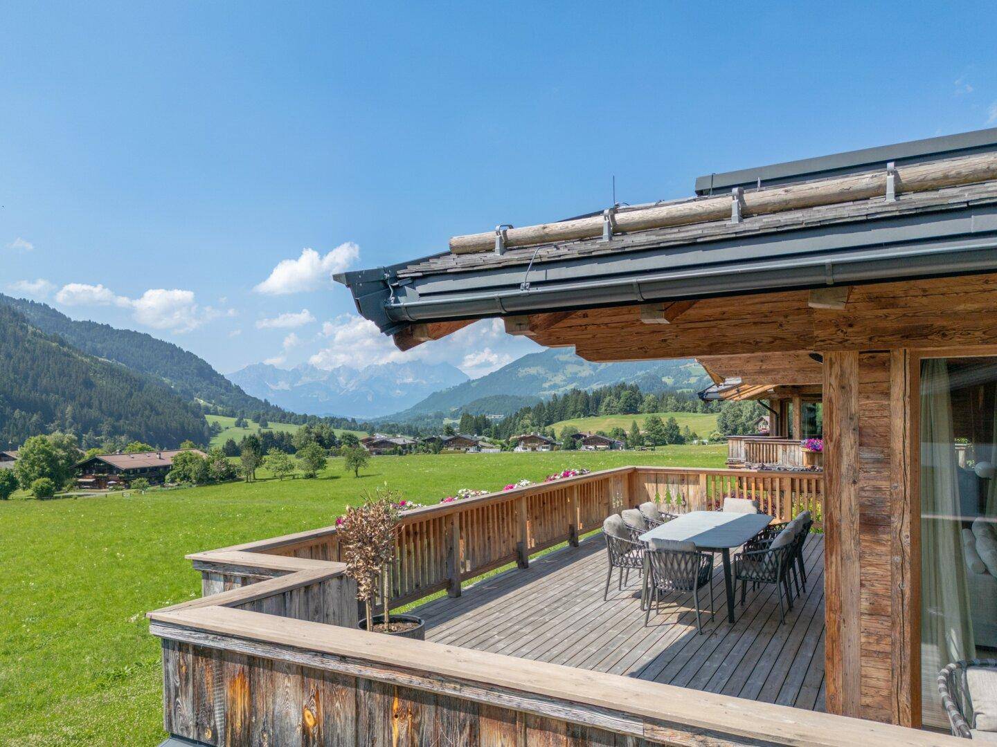 Geräumige Holzterrasse mit Esstisch und Stühlen, bietet einen weiten Blick auf die umliegende Berglandschaft.