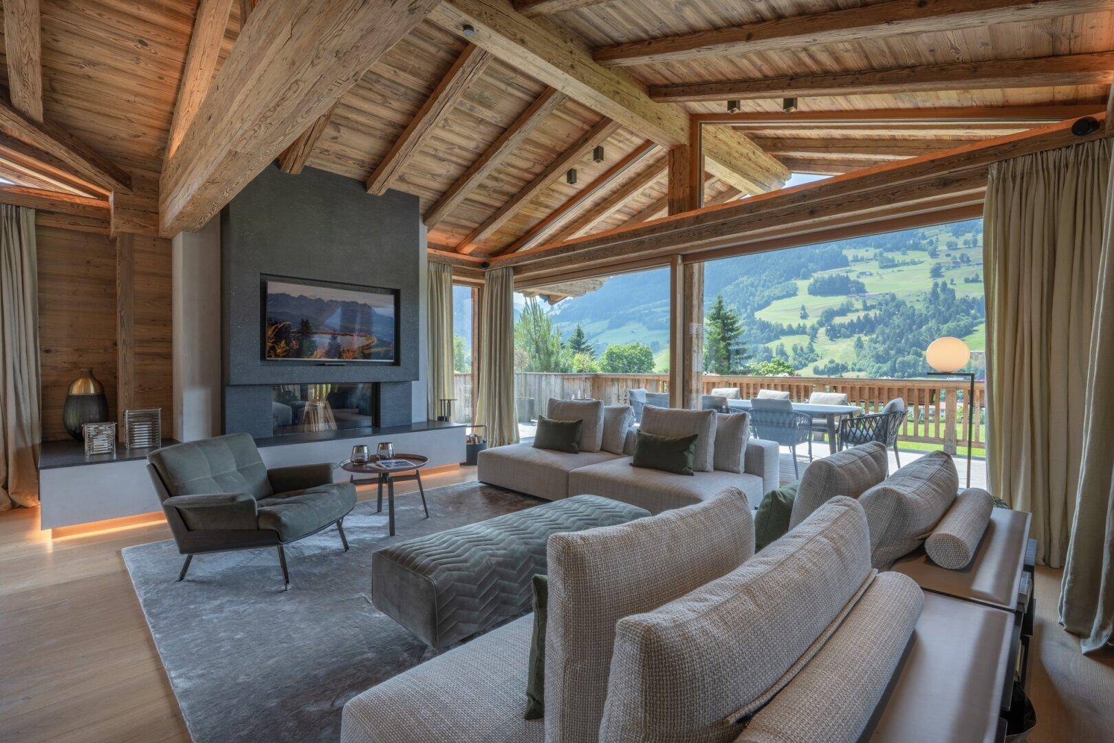 Großzügiges Wohnzimmer mit Holzbalkendecke, Kamin und bodentiefen Fenstern mit Bergblick.