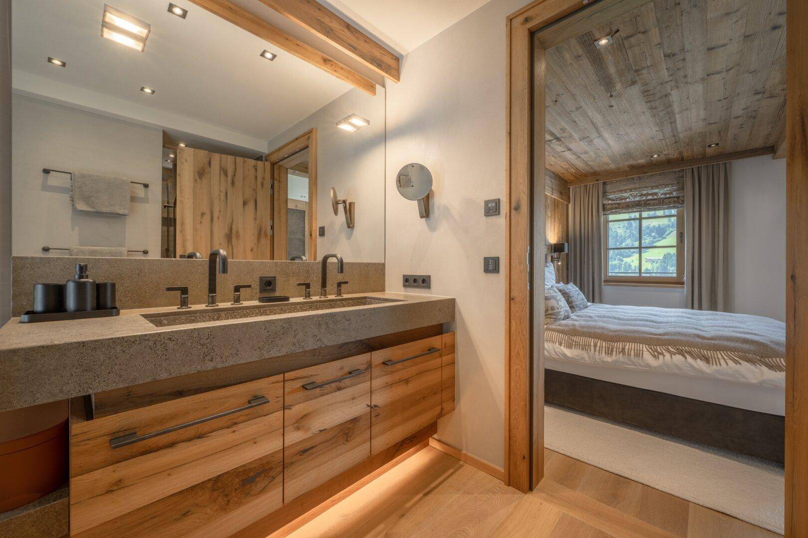 Modernes Badezimmer mit Doppelwaschbecken und Holzunterschränken, direkt vom Schlafzimmer zugänglich.