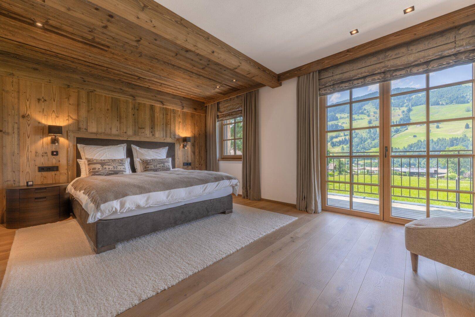 Helles Schlafzimmer mit Holzwänden, großem Bett und Balkonzugang mit Bergblick.