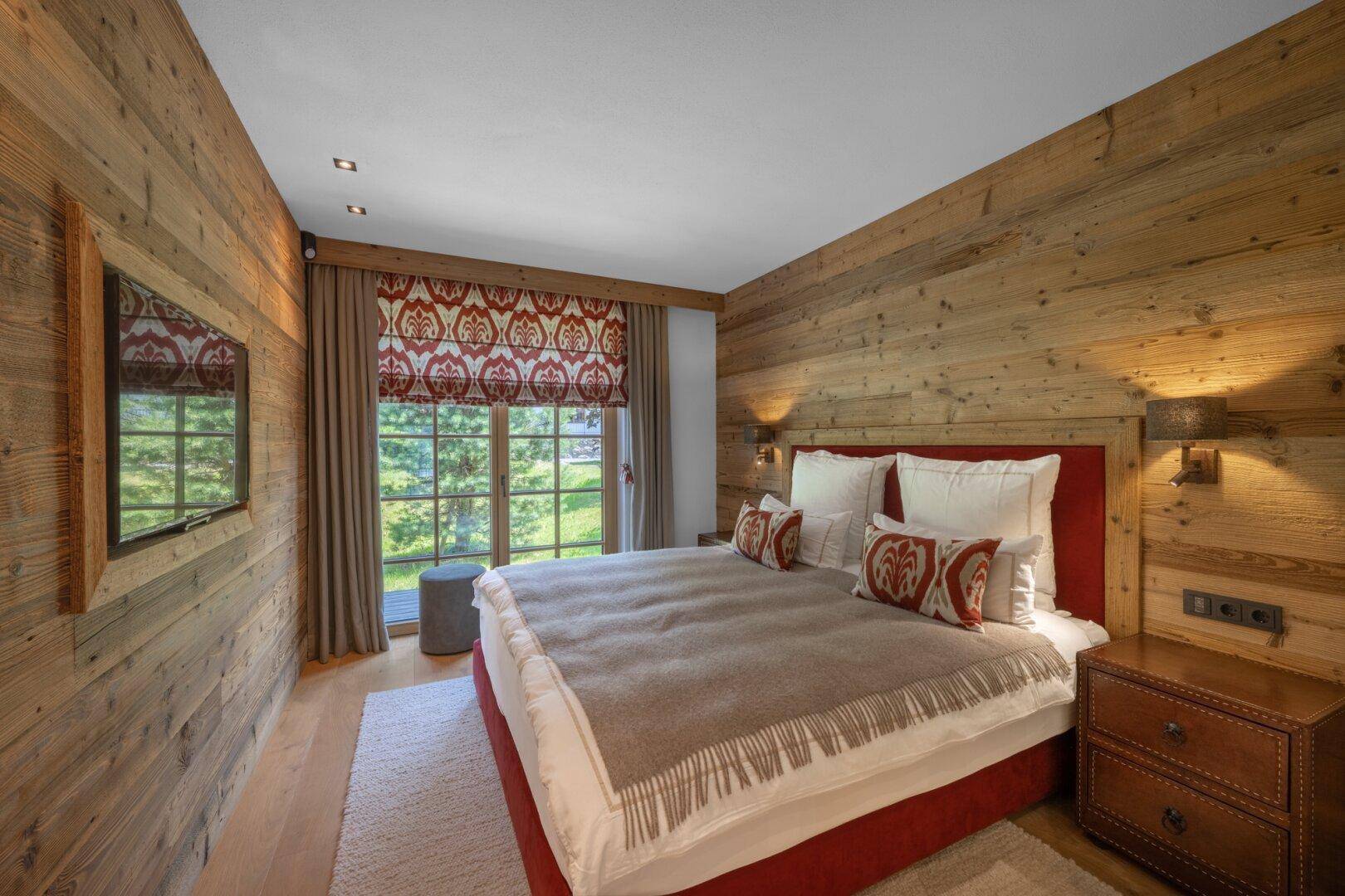 Gemütliches Schlafzimmer mit Holzwänden und rotem Bettrahmen, bietet einen ruhigen Rückzugsort.