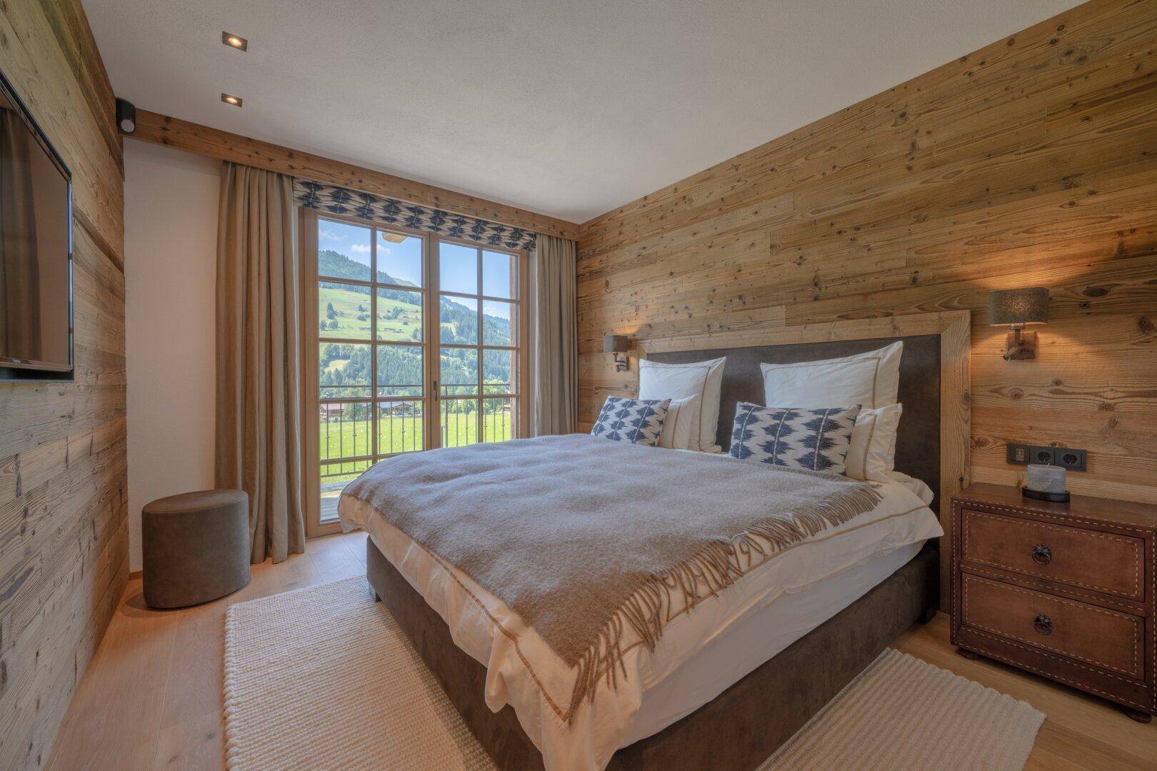 Helles Schlafzimmer mit Holzwänden und großem Fenster, das einen Blick auf die grüne Landschaft bietet.