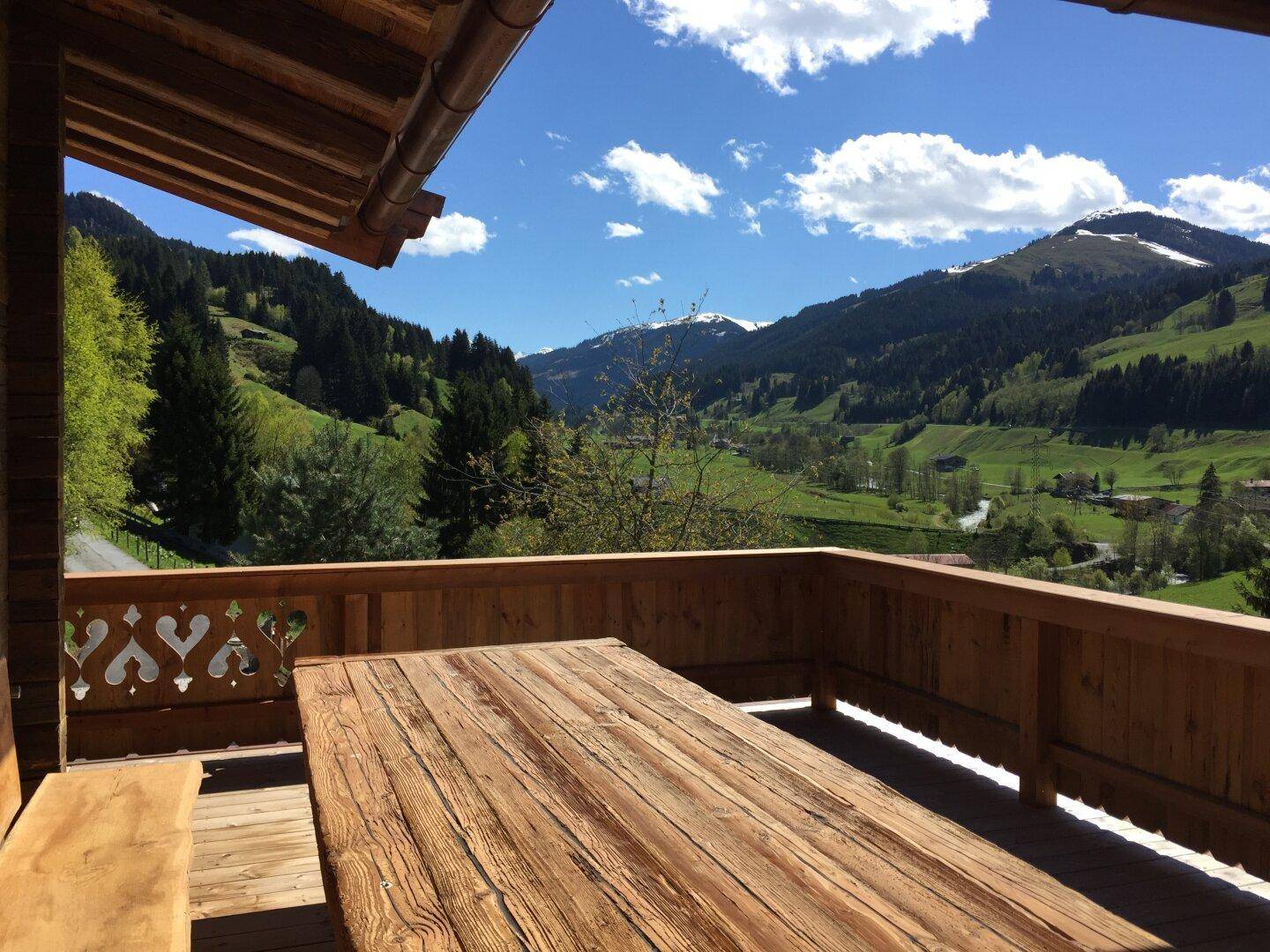 Geräumiger Holzbalkon mit Esstisch und atemberaubendem Blick auf die grünen Berge und Täler.
