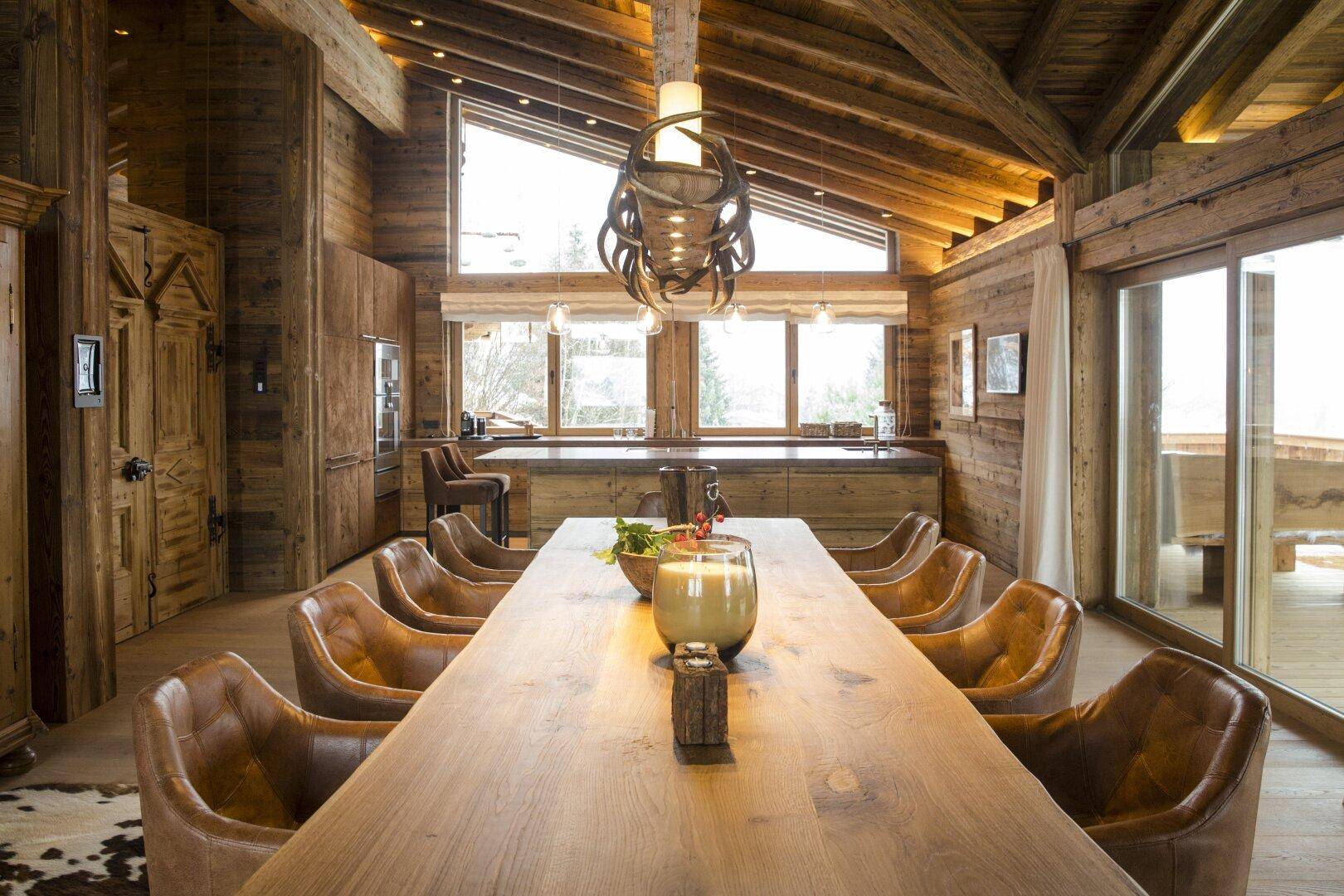 Rustikaler Essbereich mit langem Holztisch, bequemen Ledersesseln und Holzwänden unter hohen Decken.