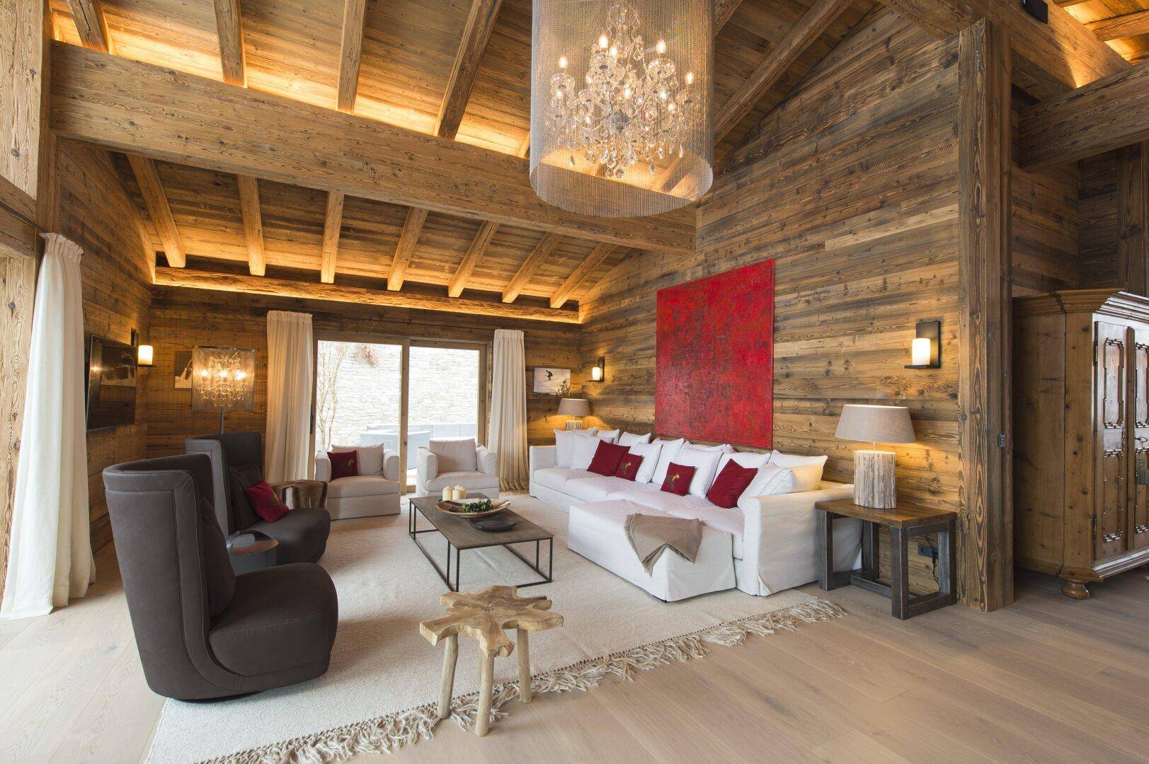 Geräumiges Wohnzimmer mit Holzwänden, weißem Sofa, Kronleuchter und Blick nach draußen.