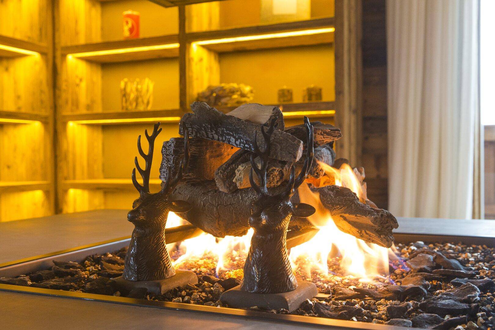 Moderner Kamin mit Hirschgeweih-Dekoration und leuchtenden Flammen, umgeben von Holzelementen.