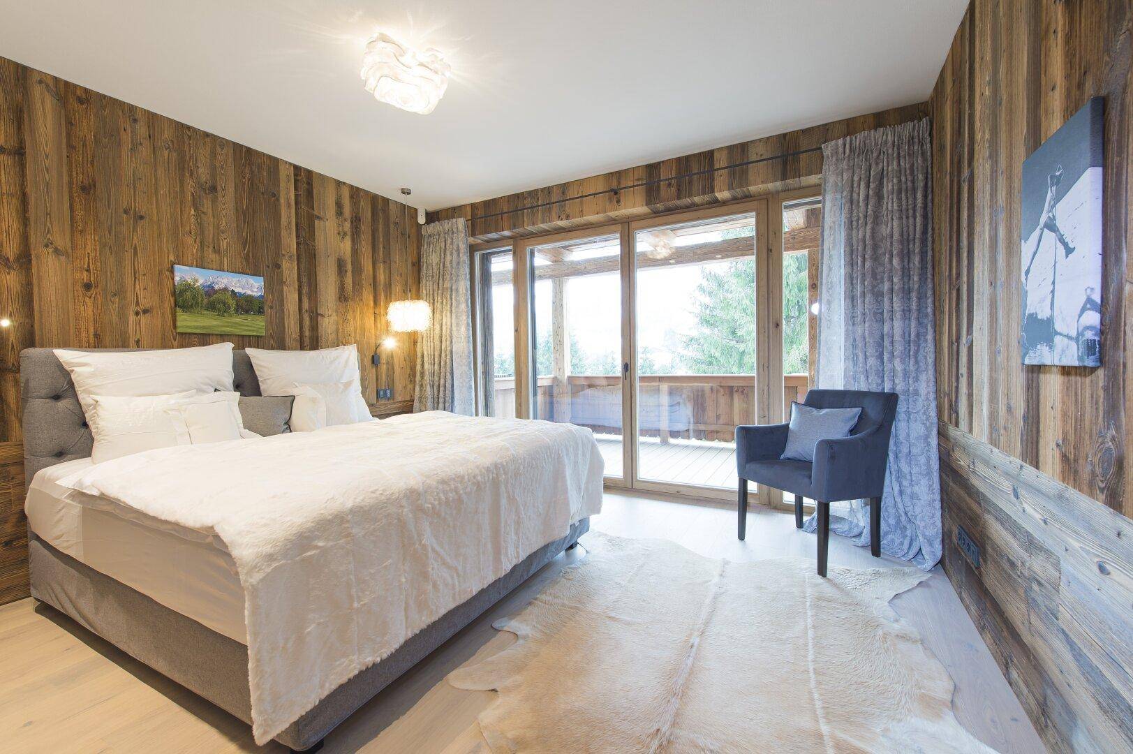 Schlafzimmer mit rustikalen Holzwänden, großem Bett und direktem Zugang zu einem Balkon.