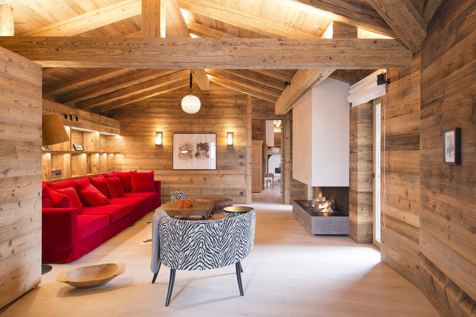 Rustikales Wohnzimmer mit rotem Sofa, Holzbalken und modernem Kamin in einem offenen Raumkonzept.
