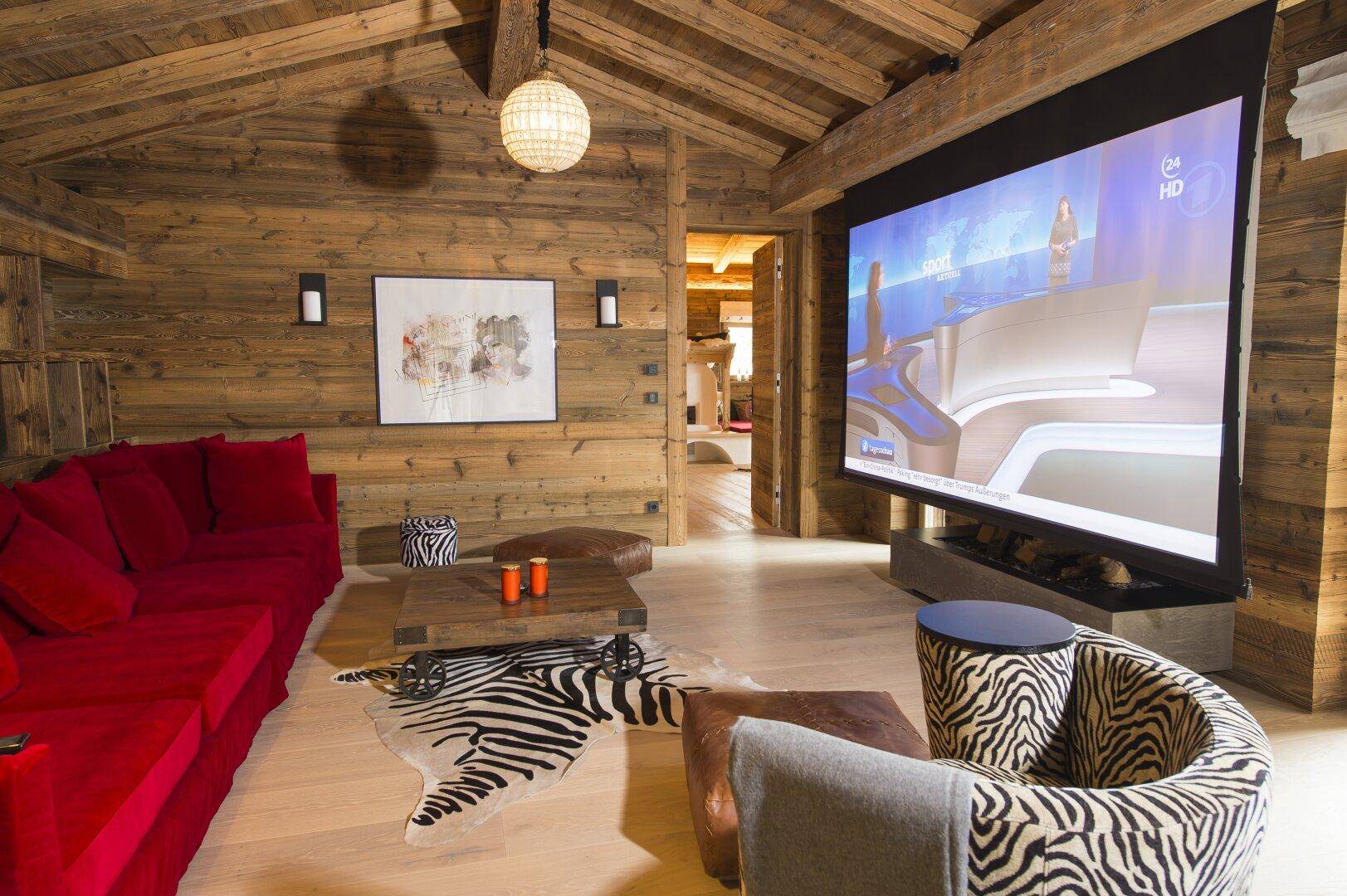 Medienraum mit großem Projektionsbildschirm, rotem Sofa und rustikalem Holzinterieur unter Holzbalken.
