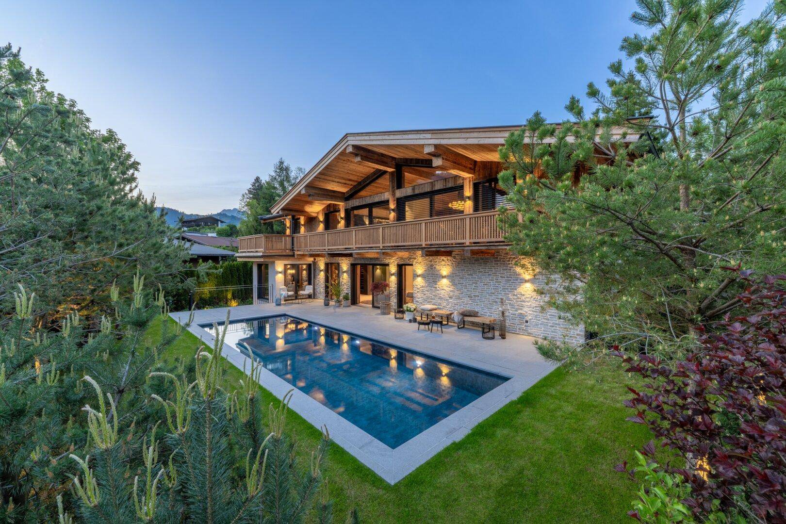 Elegantes Chalet mit großem Außenpool und weitläufiger Terrasse, eingebettet in eine grüne Landschaft.