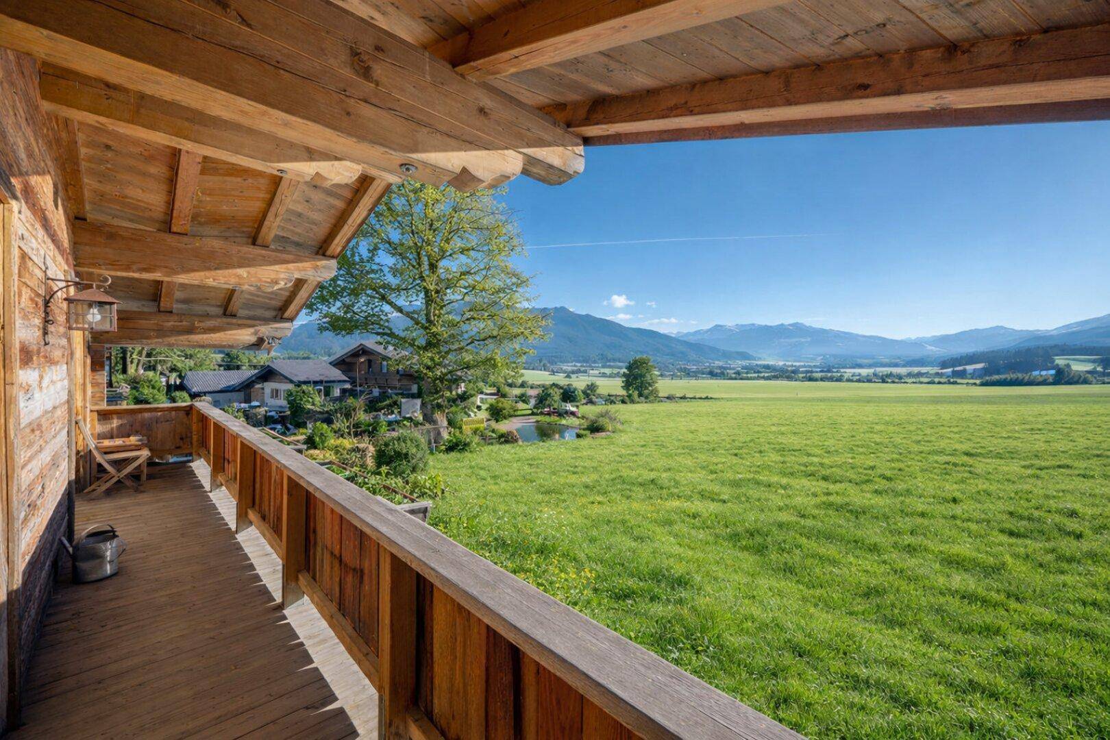 Holzbalkon mit weitem Blick über grüne Felder und die umliegende Berglandschaft.