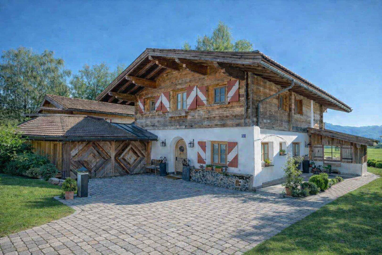Traditionelles Chalet mit Holzfassade, weißen Wänden, roten Fensterläden und gepflasterter Auffahrt.