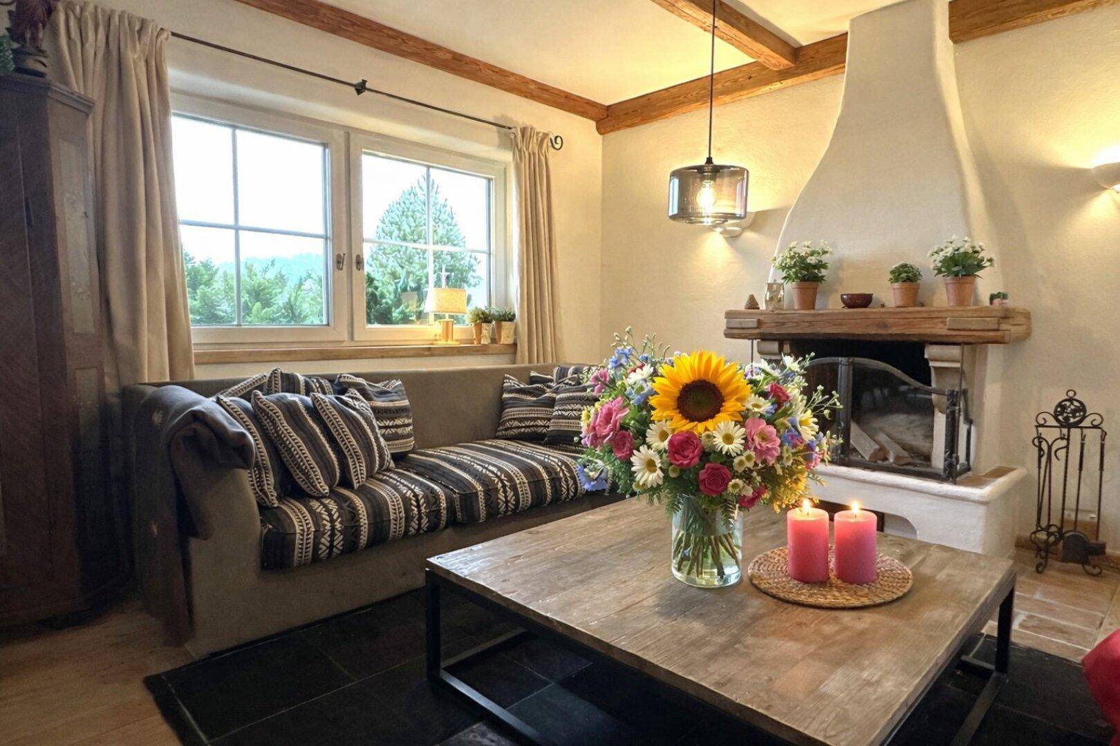 Helles Wohnzimmer mit Kamin, bequemer Couch und großen Fenstern mit weitem Blick ins Grüne.