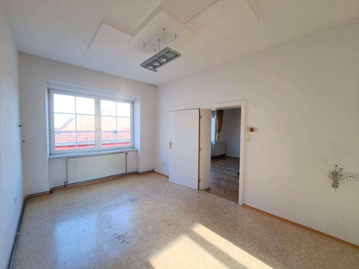 Geräumiges Zimmer mit hellem Linoleumboden und großem Fenster, das viel Sonnenlicht einfängt.