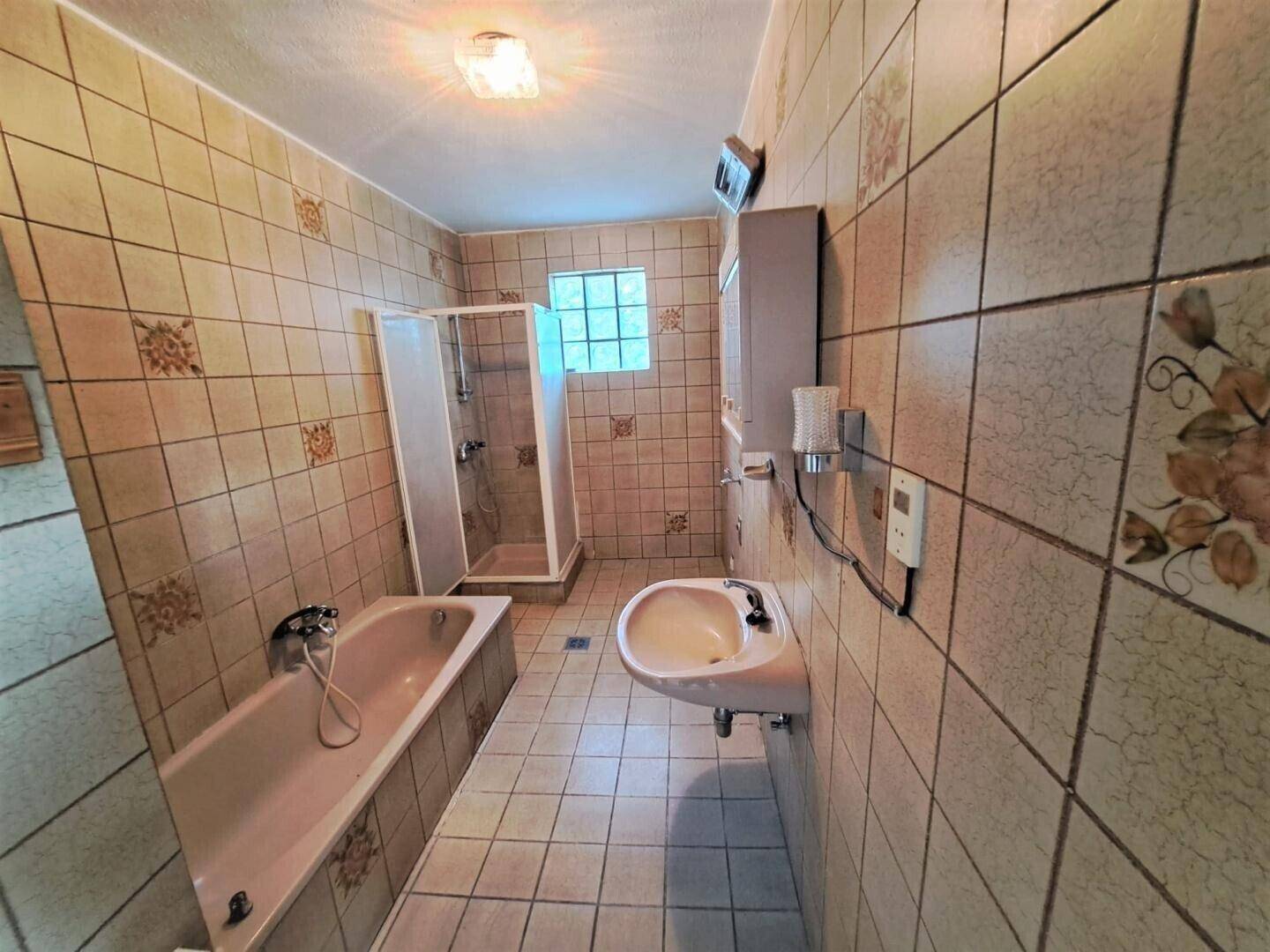 Badezimmer mit Badewanne, Dusche und Waschbecken, gefliest in warmen Beigetönen.