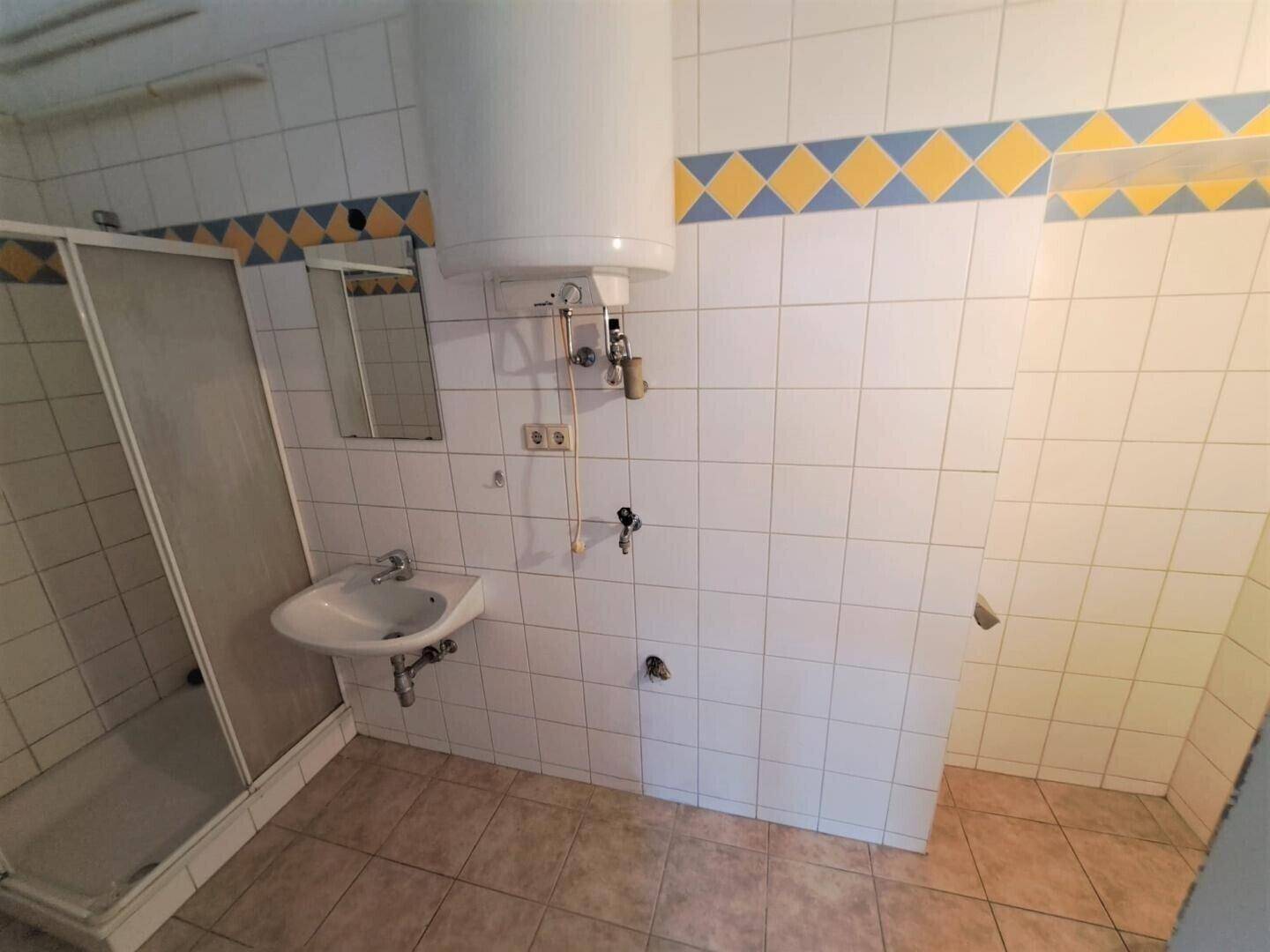 Badezimmer mit Duschkabine und Waschbecken, gefliest mit weißen und farbigen Akzenten.