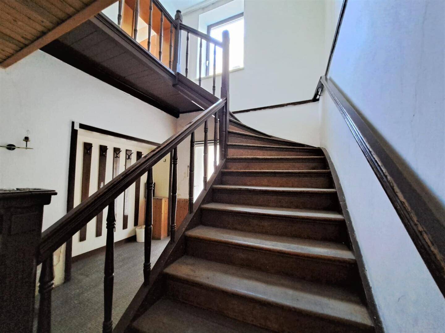 Klassisches Holztreppenhaus mit Geländer und natürlichem Lichteinfall durch ein Fenster.