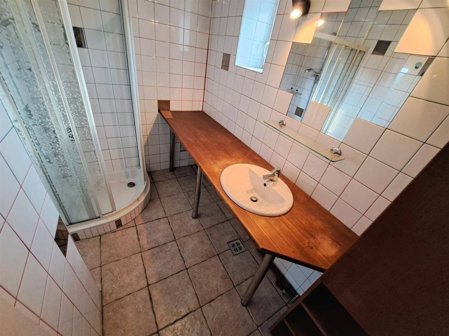 Modernisiertes Badezimmer mit Duschkabine, Holzwaschtisch und weißen Fliesen.