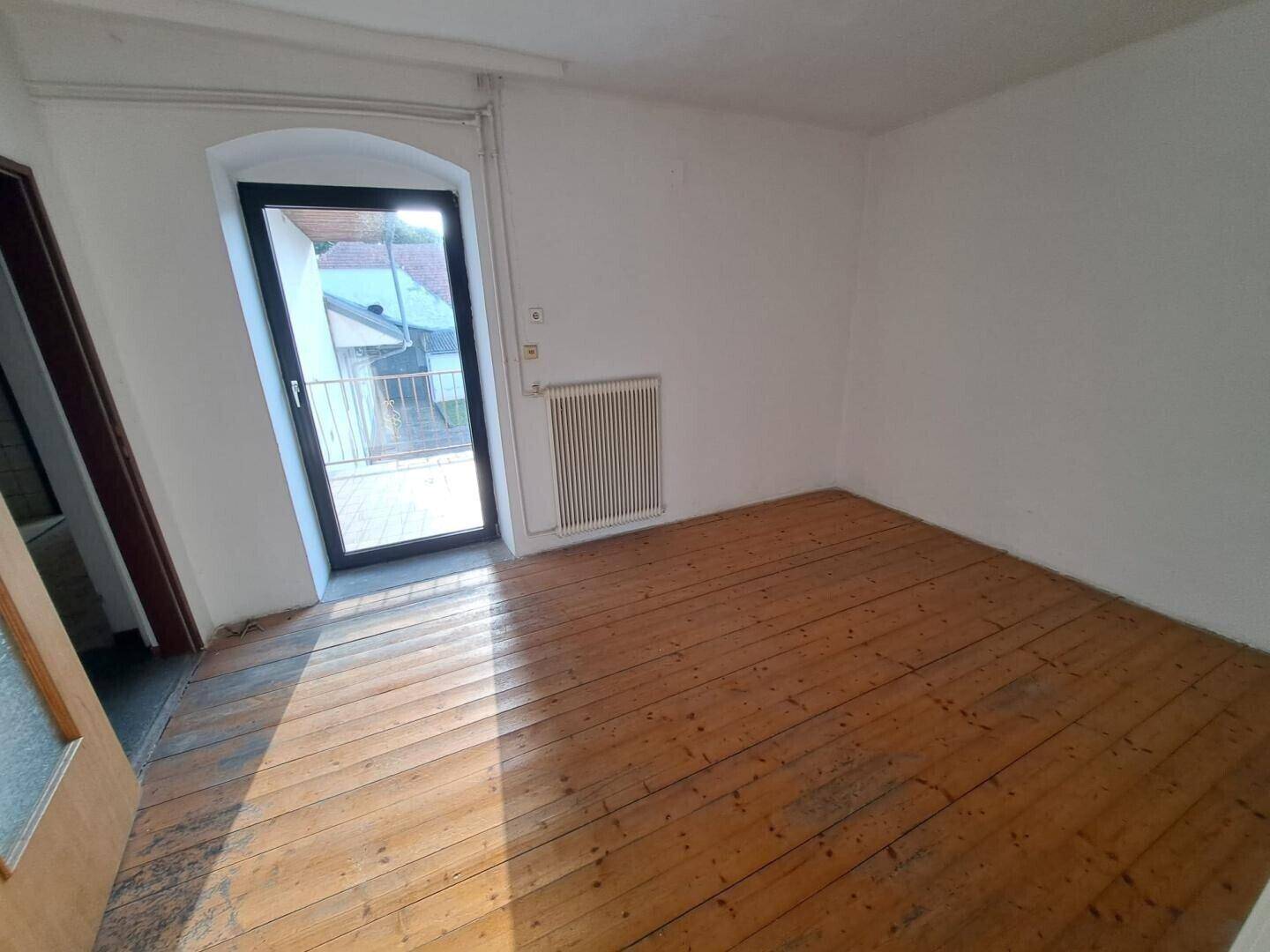 Helles Zimmer mit Dielenboden und Zugang zu einem kleinen Balkon oder einer französischen Brüstung.
