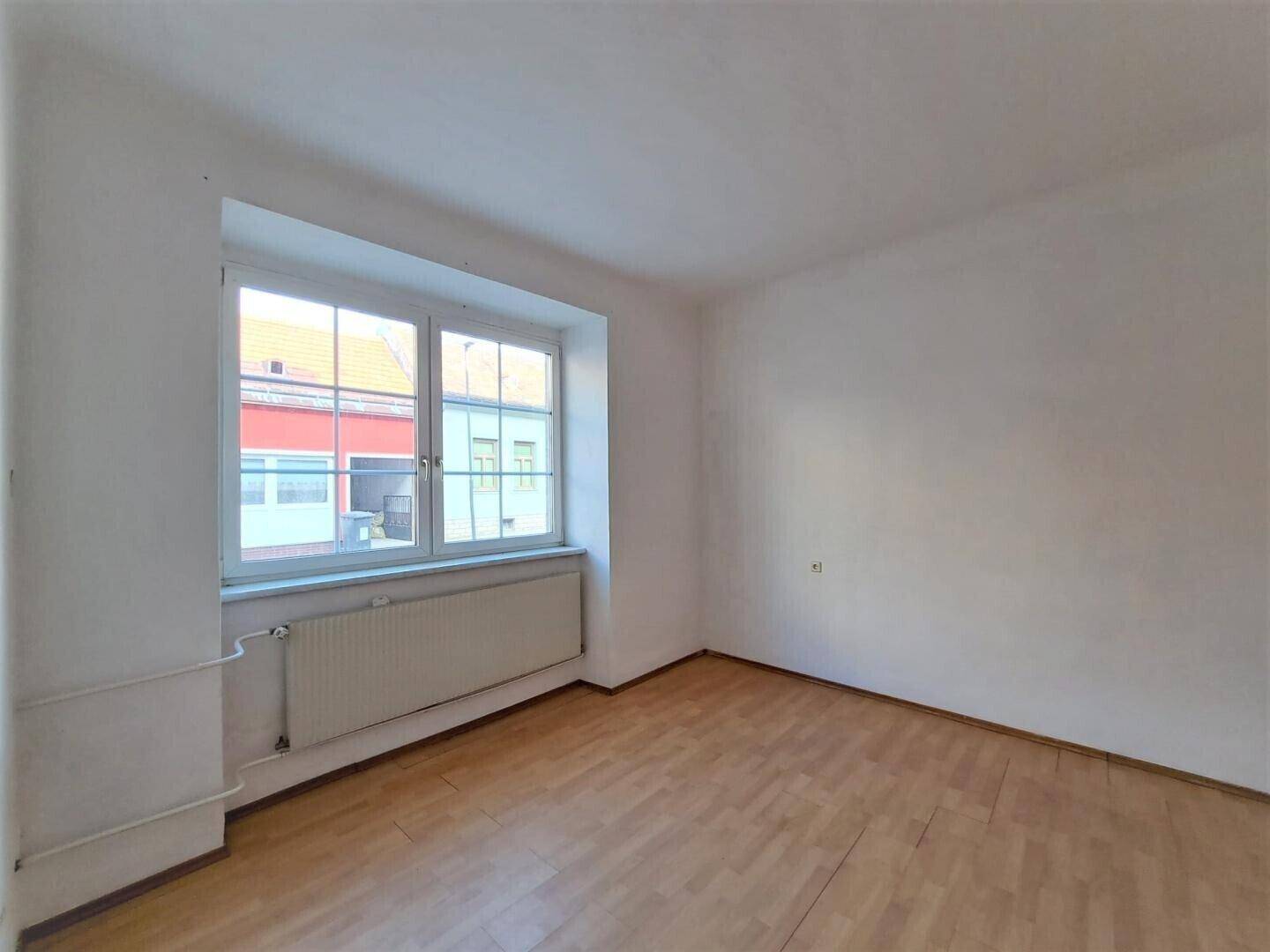 Helles Zimmer mit Holzparkettboden und großem Fenster, das viel Tageslicht hereinlässt.