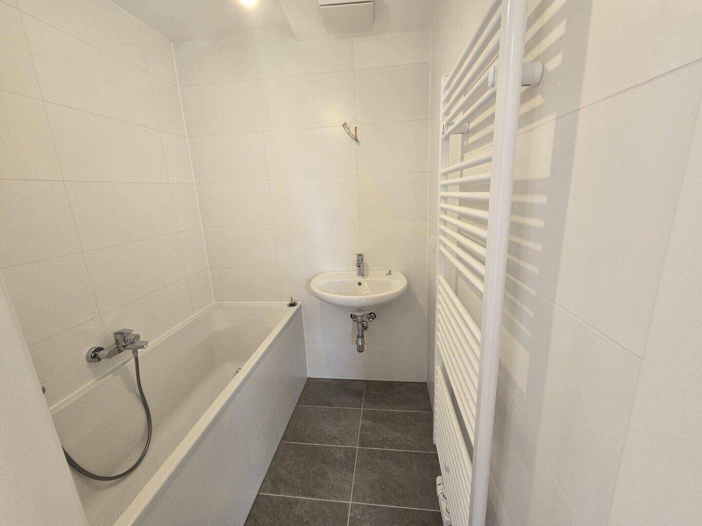 Helles Badezimmer mit Badewanne, Waschbecken und beheiztem Handtuchhalter, ausgestattet mit modernen Fliesen.