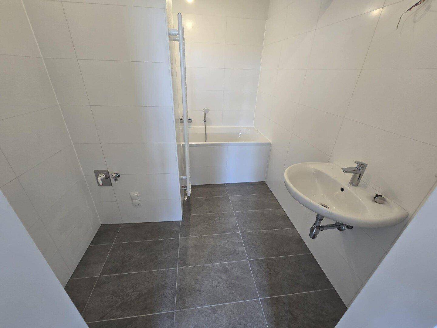 Funktionales Badezimmer mit Badewanne, Waschbecken und grauen Bodenfliesen.