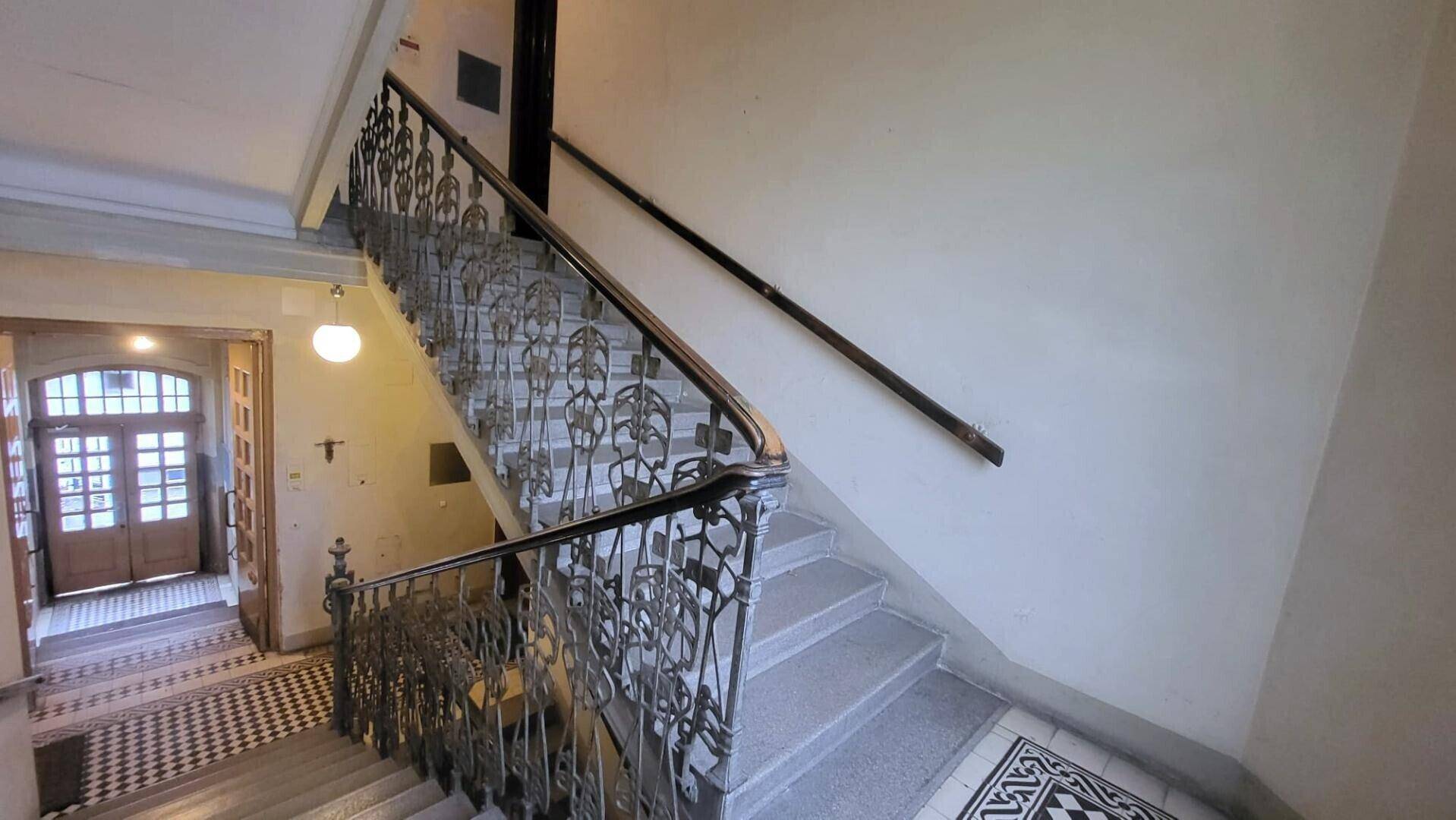 Historisches Treppenhaus mit kunstvollen Geländern, Steinstufen und gemustertem Fliesenboden im Eingangsbereich.