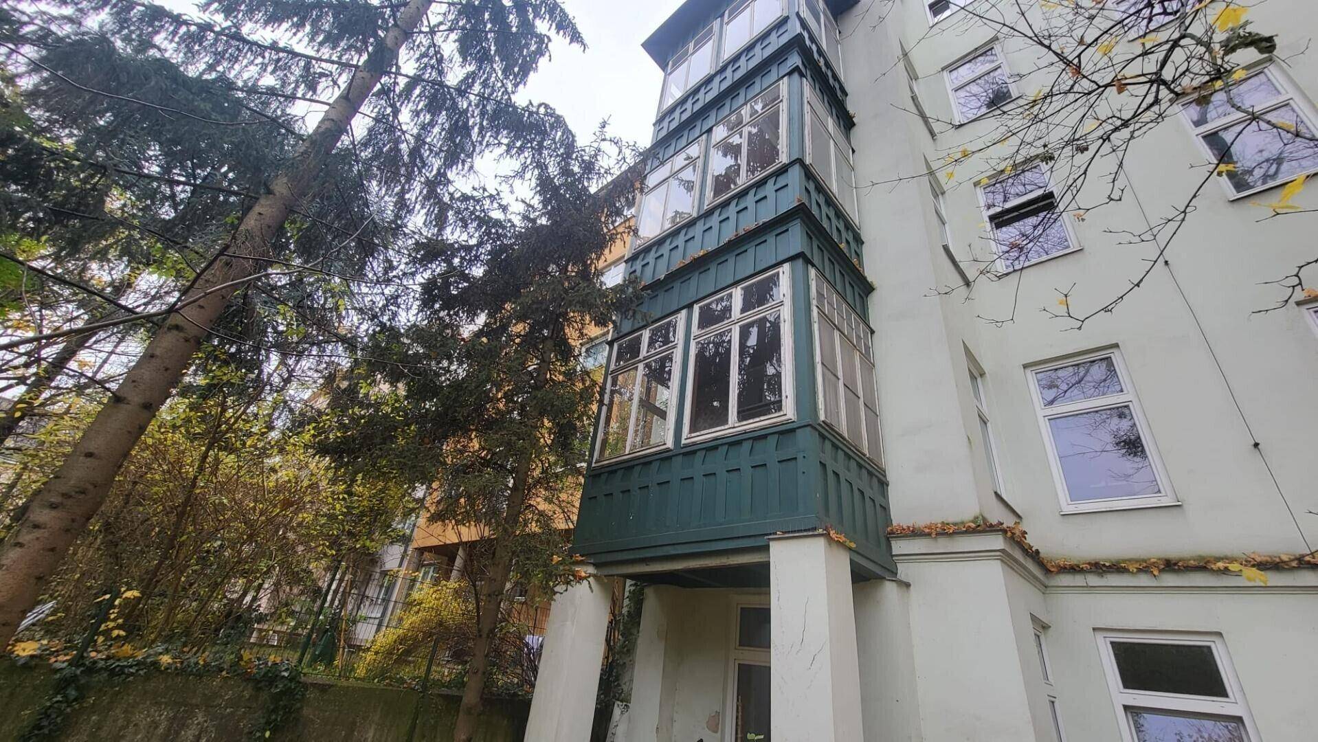 Historische Fassade eines Gebäudes mit markantem grünen Erker und umgebenden Bäumen.