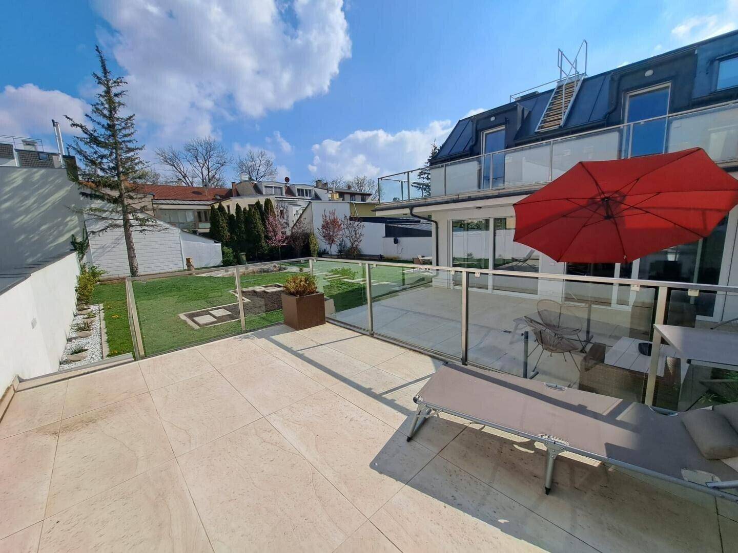 Große, sonnige Terrasse mit Fliesenboden, Liegestuhl und Blick auf den Garten.