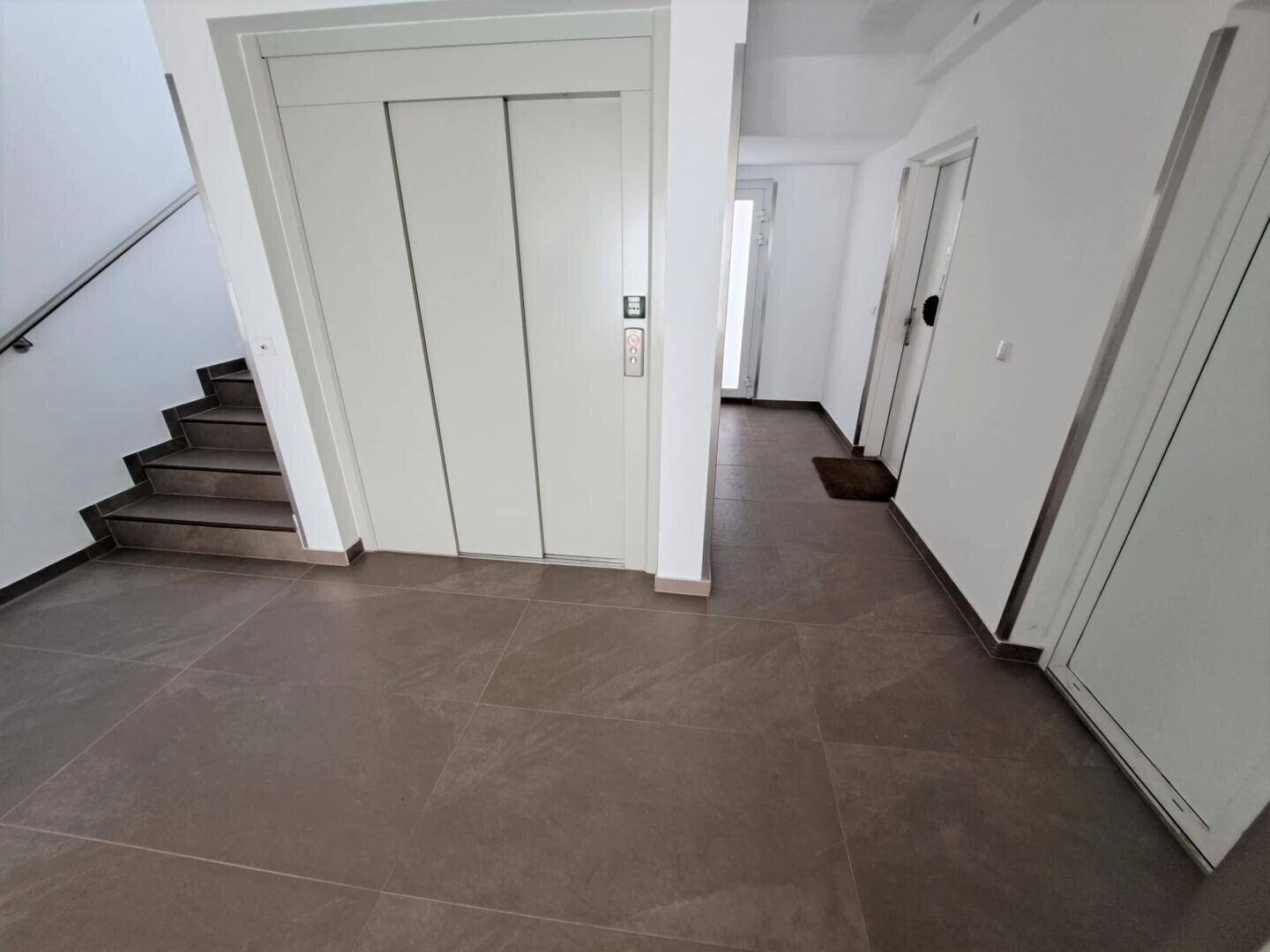 Heller Eingangsbereich mit Aufzug und Treppenhaus, modern und funktional gestaltet.
