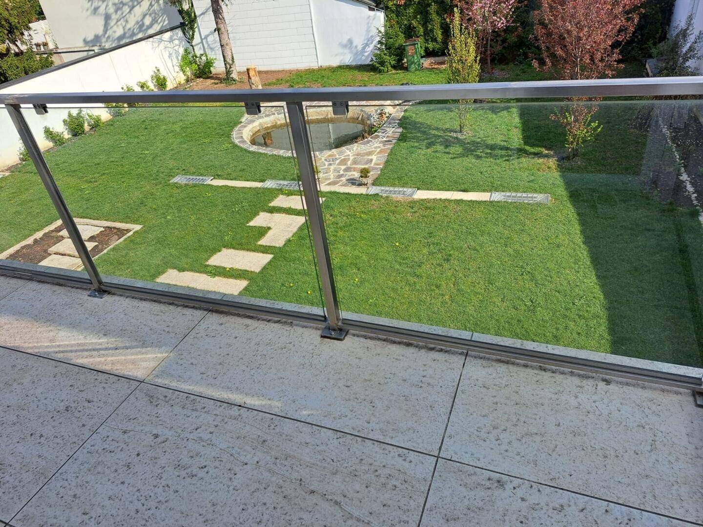 Terrasse mit Fliesenboden und Blick auf den grünen Garten mit Teich.