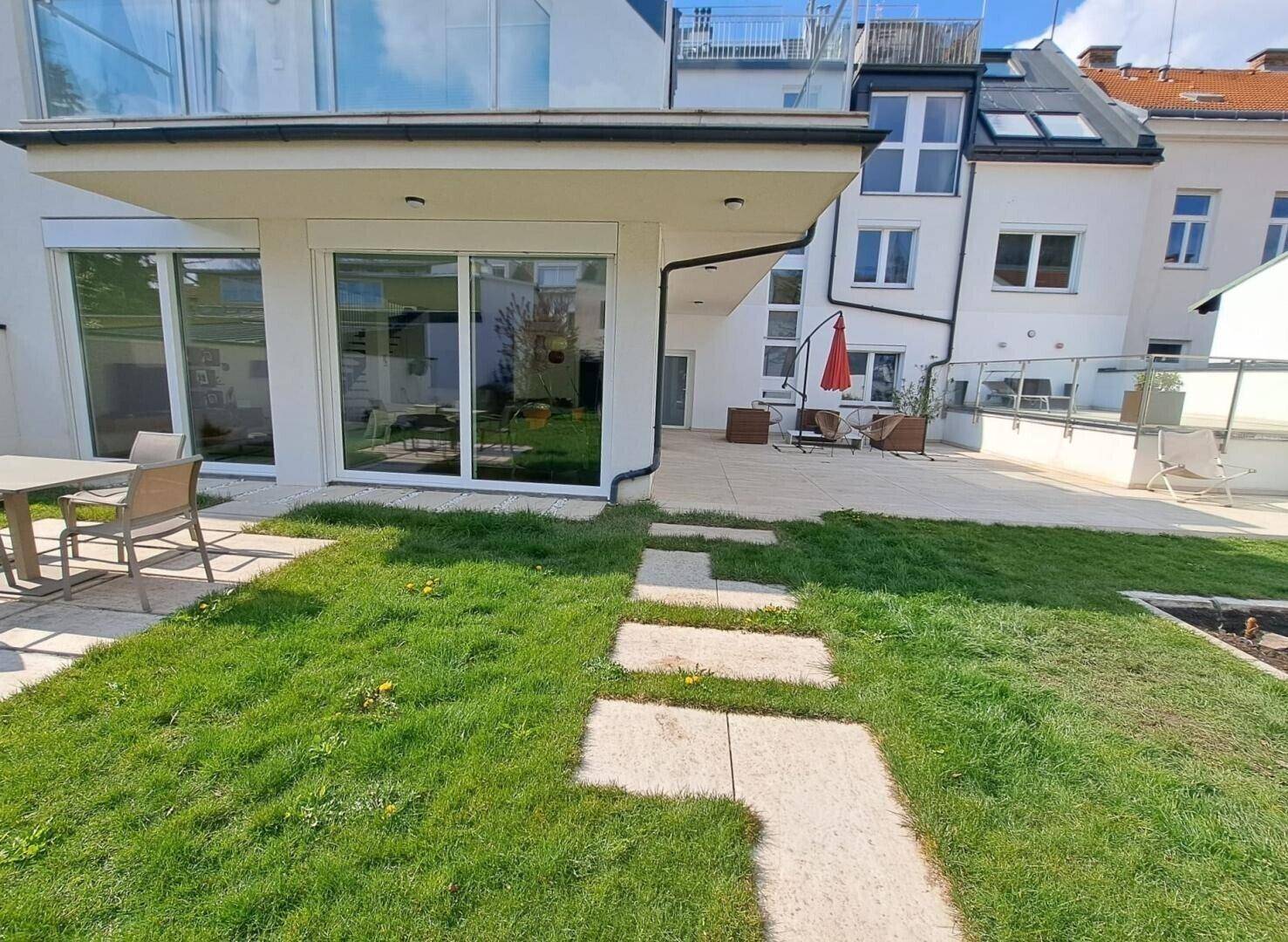 Gepflegter Garten mit Rasenfläche, Steinplattenweg und angrenzender Terrasse.